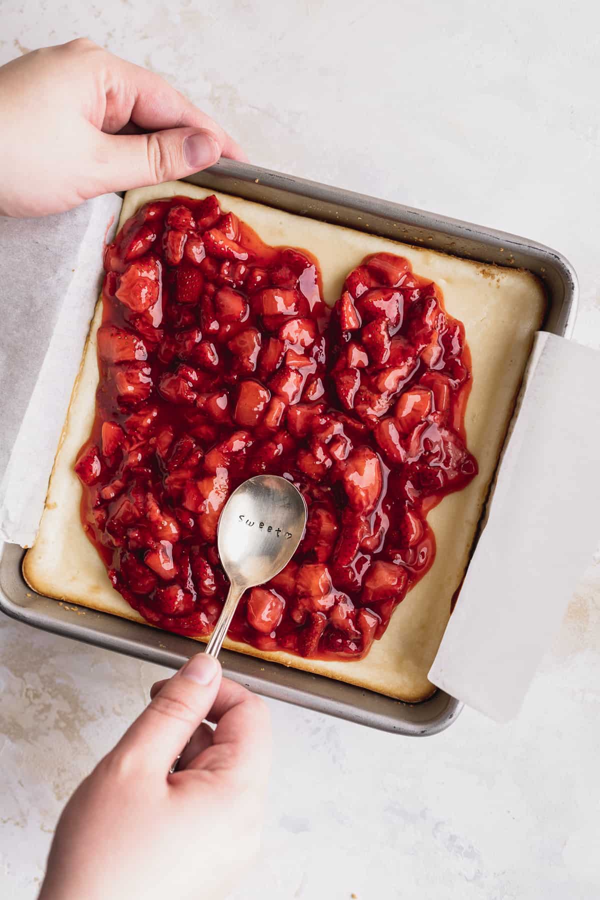 Spreading strawberry sauce on top of baked cheesecake.