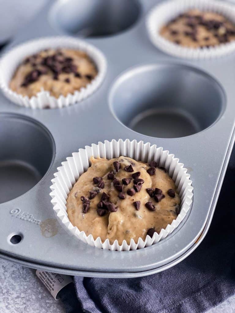 The batter of peanut butter banana muffins in the muffin tin with extra mini chocolate chips on top