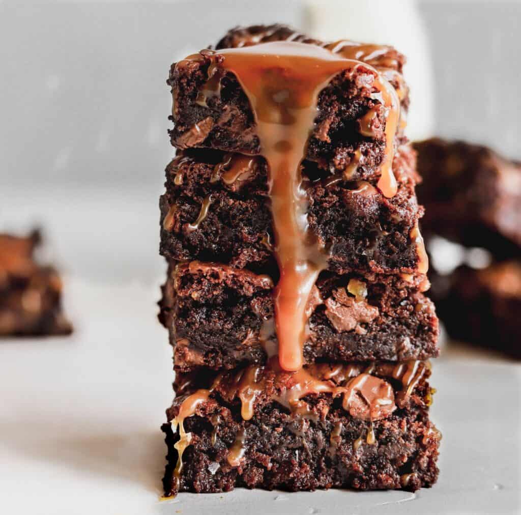 Salted caramel fudge brownies stacked up 4 high with salted caramel from scratch dripping down.