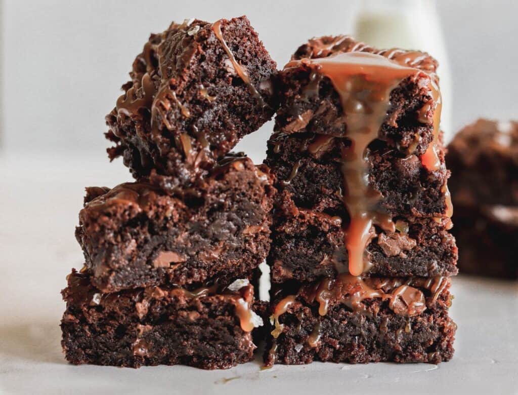 A huge stack of salted caramel fudge brownies with caramel dripping down.