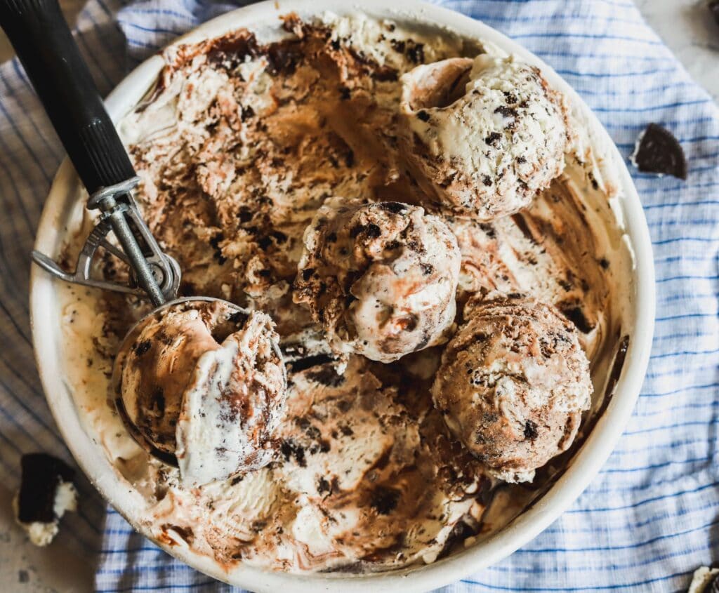 Easy no-churn oreo and hot fudge ice cream in a pan with scoops showing.