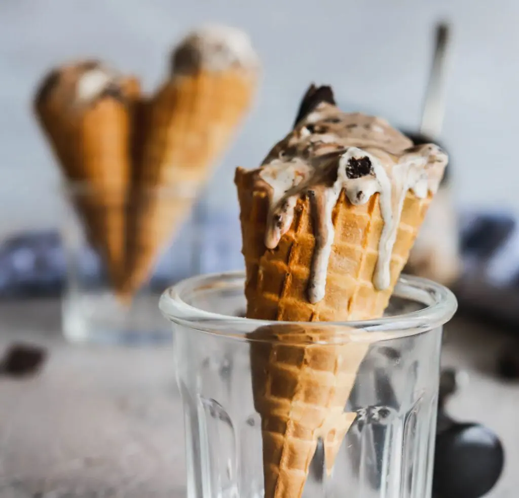 no-churn oreo and hot fudge ice cream made with no machine in a waffle cone with ice cream dripping down the sides.