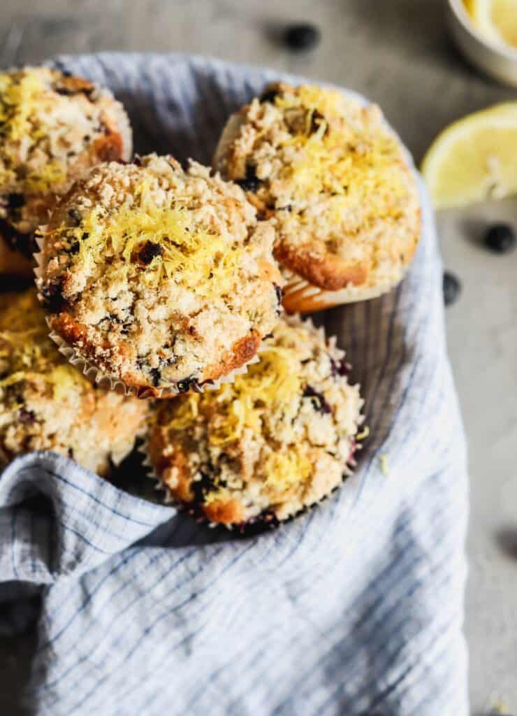 Lemon blueberry muffins that have a crumb topping in a bowl with a napkin.
