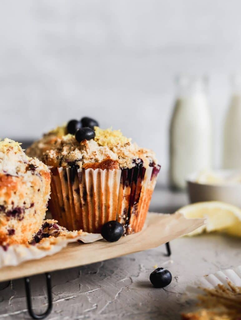 Lemon blueberry muffins with a zesty crumb topping on a cooling rack with a milk jug in the back.