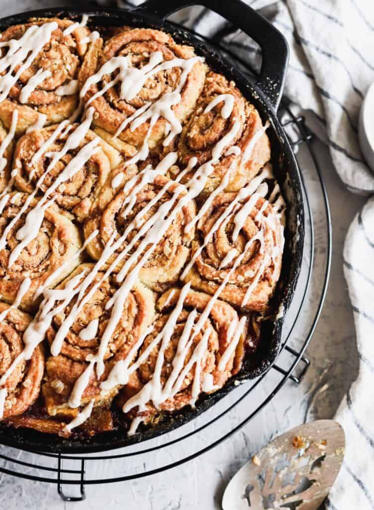 Peach cobbler with cinnamon swirl biscuits with the cinnamon cream cheese glaze on top in a cast iron.