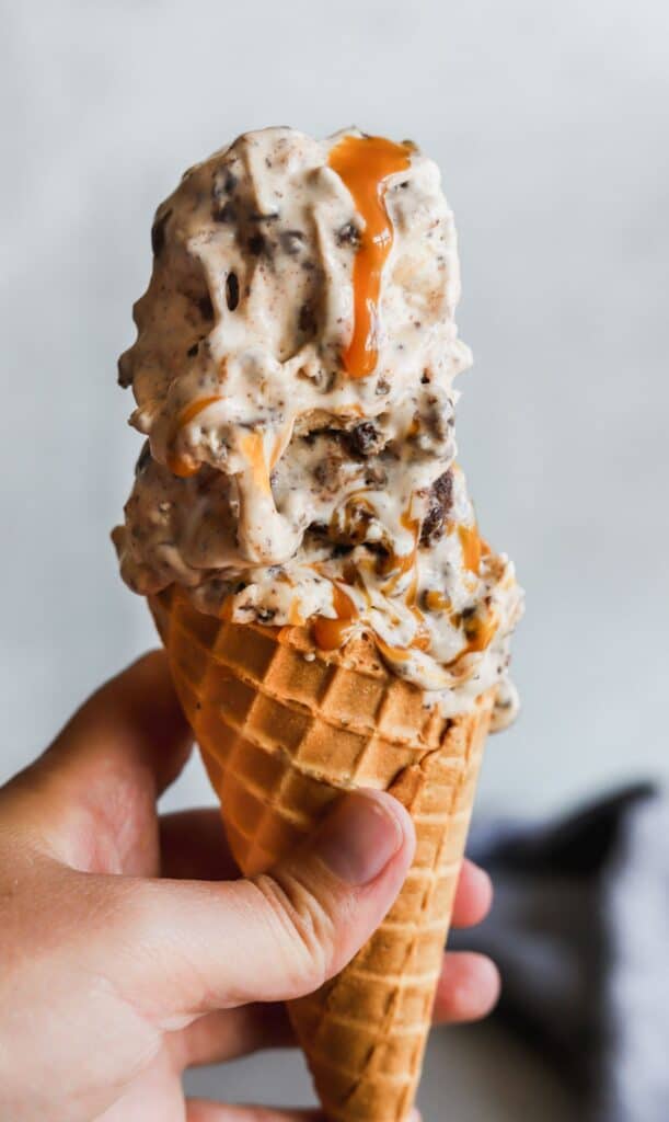 No churn salted caramel brownie ice cream in a waffle cone with a drip of homemade caramel running down.