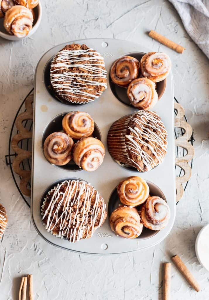 Jumbo cinnamon roll muffins in a muffin tin with little mini cinnamon rolls on the side.