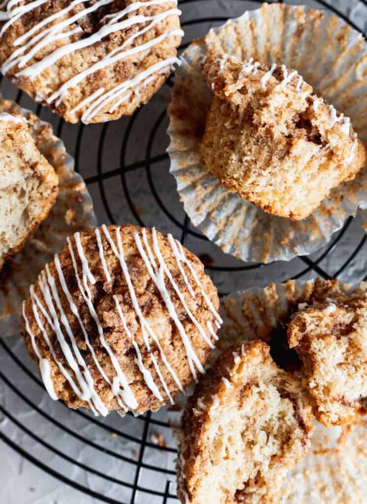 CInnamon roll muffins with cream cheese glaze on a wire cooling rack with several muffins on theirs sides.