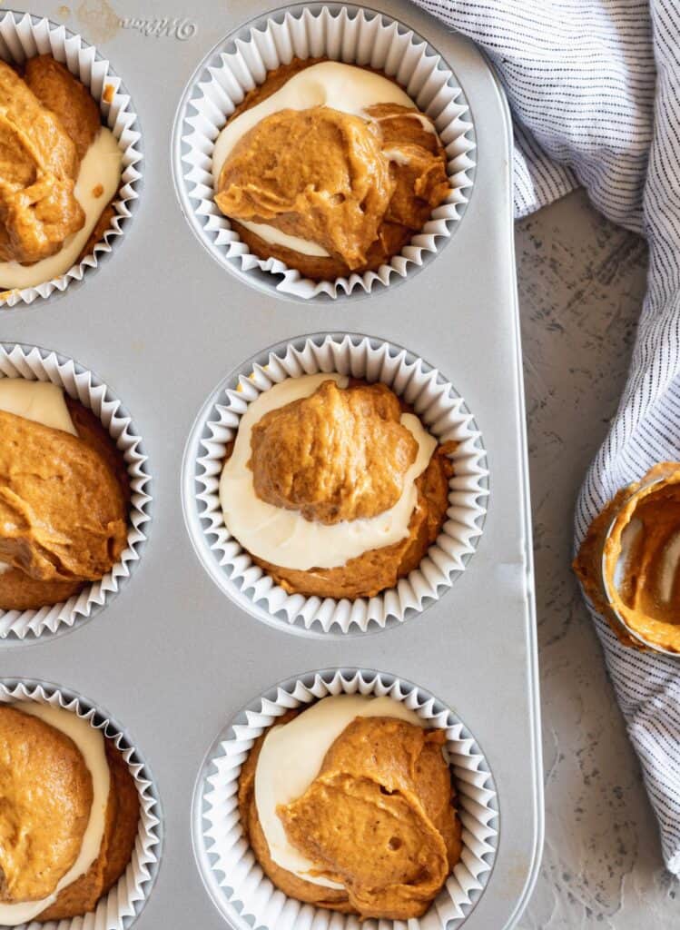 Pumpkin cheesecake muffin batter swirled together in a muffin tin.