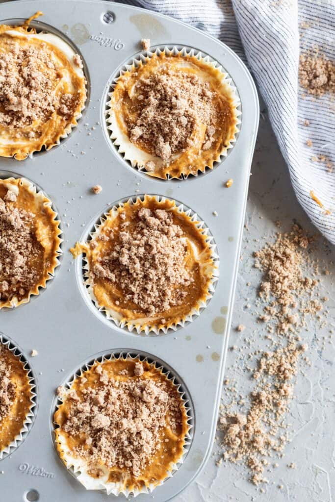 Pumpkin cheesecake muffins with cinnamon crumb topping on top in a muffin tin.