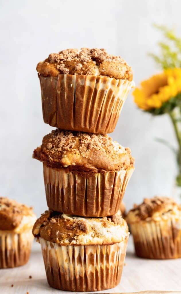 A stack of 3 pumpkin cheesecake swirl muffins stacked on top of each other.
