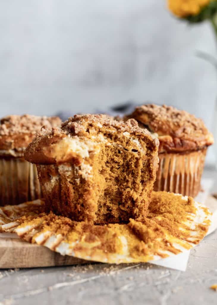 A pumpkin cheesecake swirl muffin with a big bite take out of it on a wooden board.