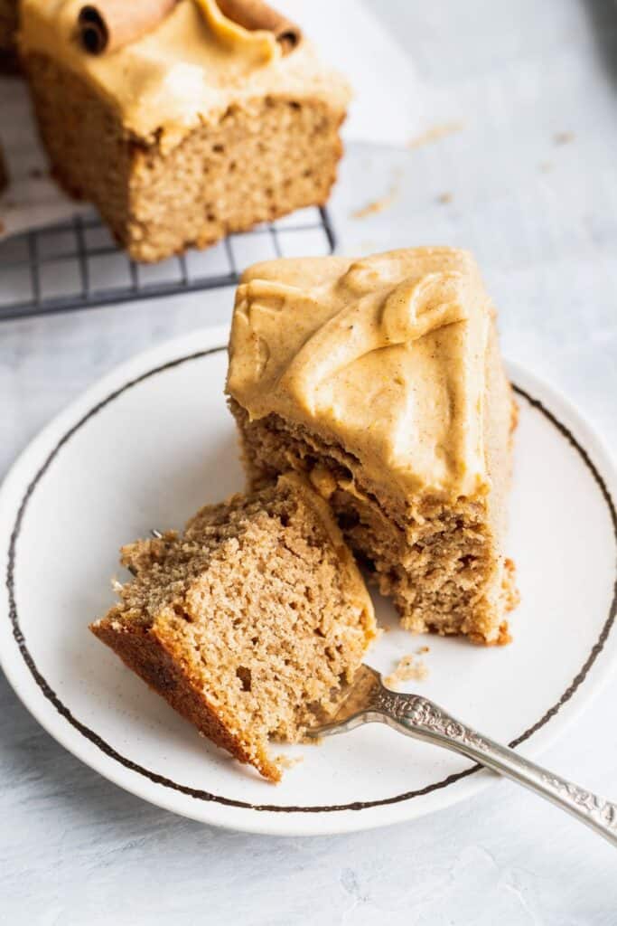 1 slice of spice sheet cake with pumpkin frosting on a plate with a bite missing.