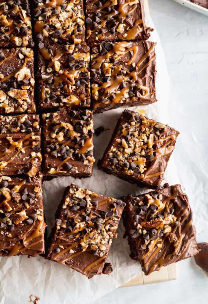 A few salted caramel turtle brownies spread around on parchment paper.