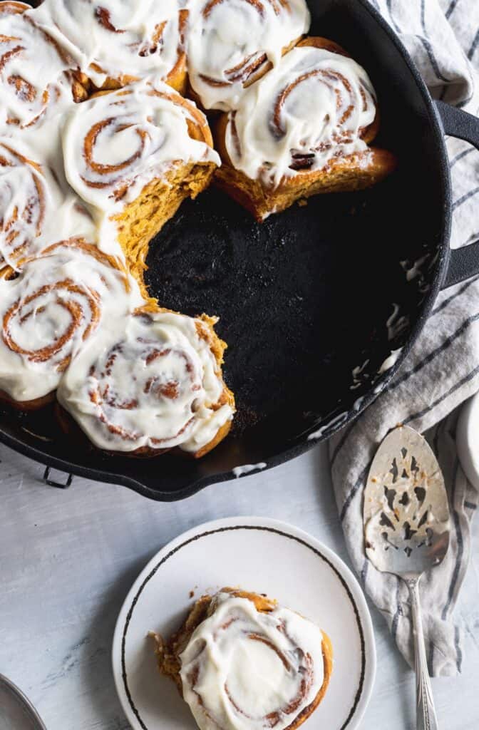 Pumpkin spice cinnamon rolls in a cast iron pan with a few missing.