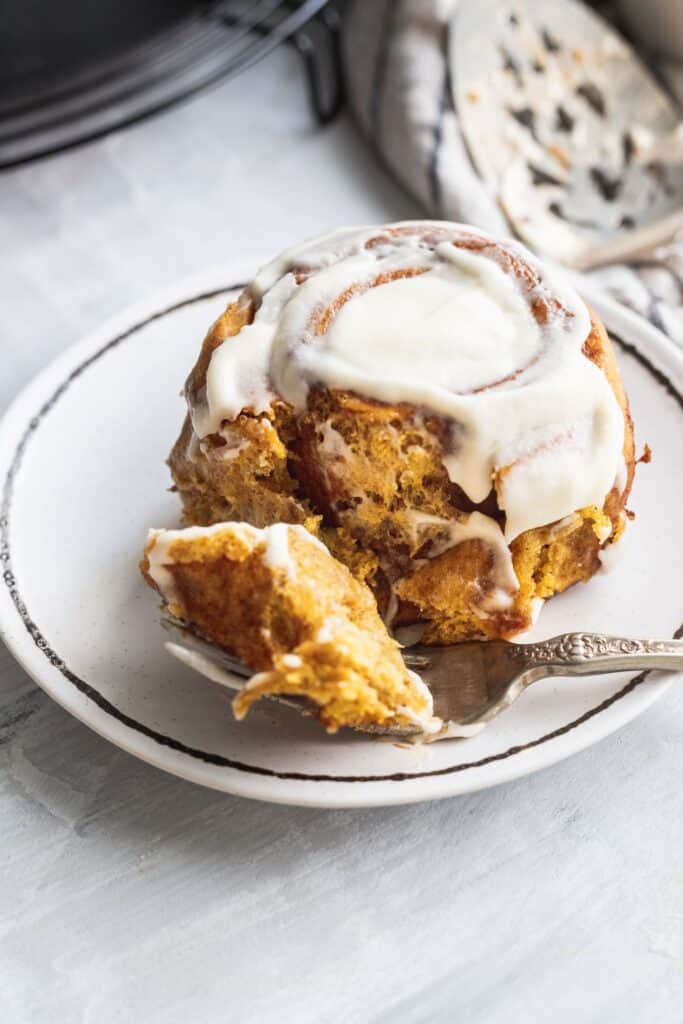 1 pumpkin spice cinnamon roll on a plate with a bite missing.