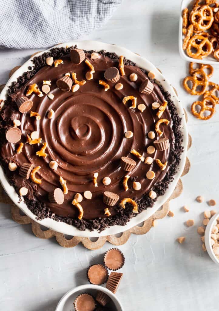 Chocolate peanut butter cup pie in a pie dish with pretzels, and peanut butter cups scattered around