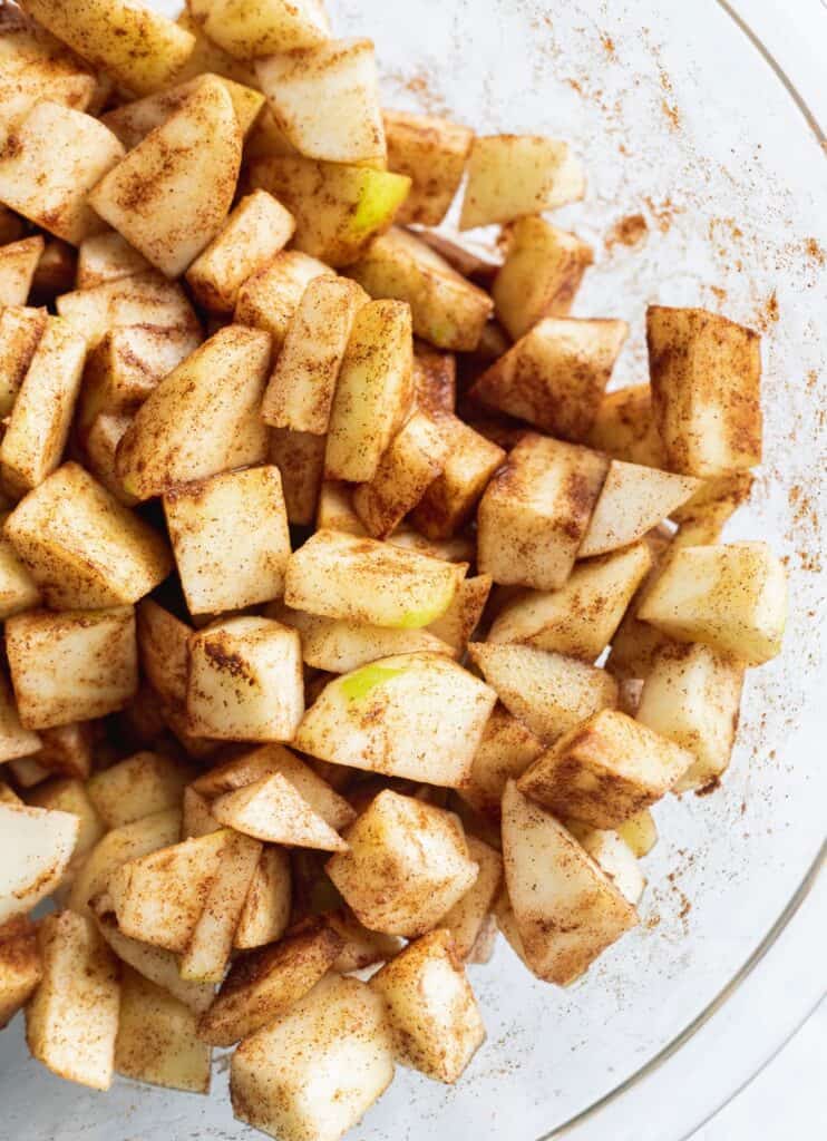 Sliced apples with cinnamon mixture in a glass bowl.