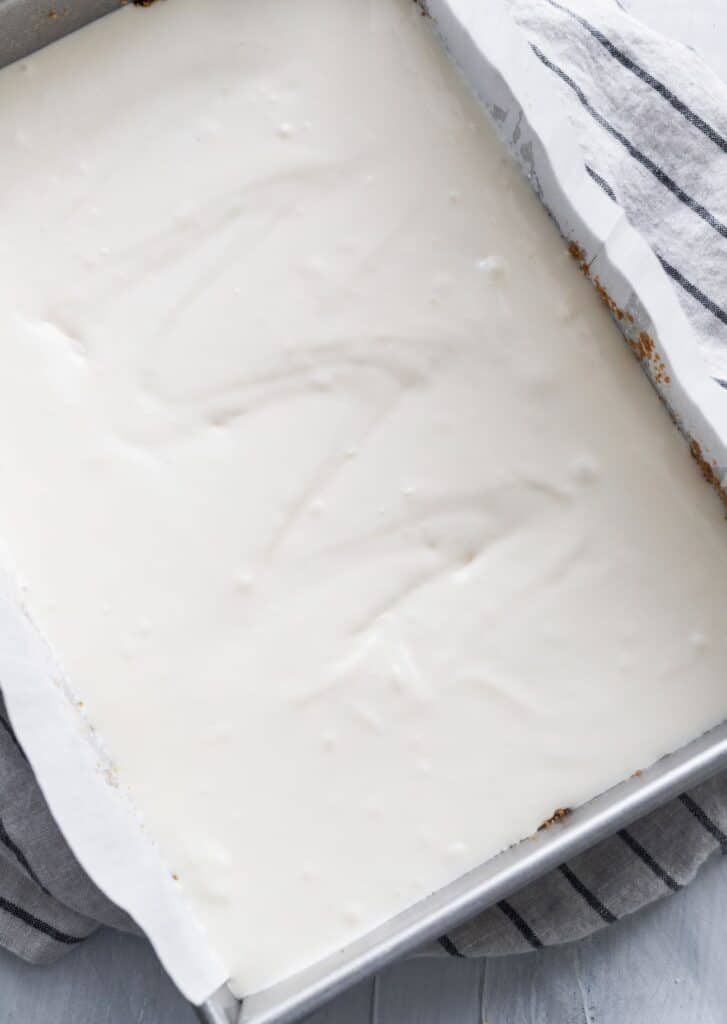 Cheesecake batter on top of graham cracker crust in metal pan.