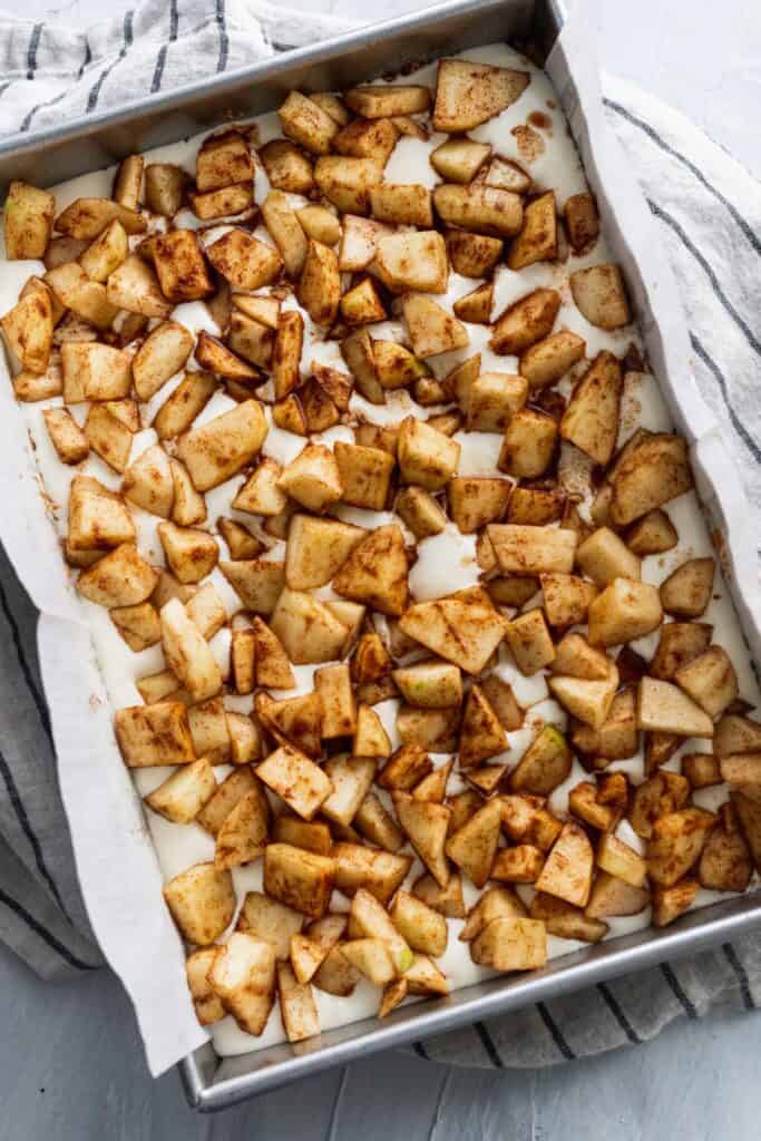 Sliced apples on top of cheesecake batter in a metal pan.