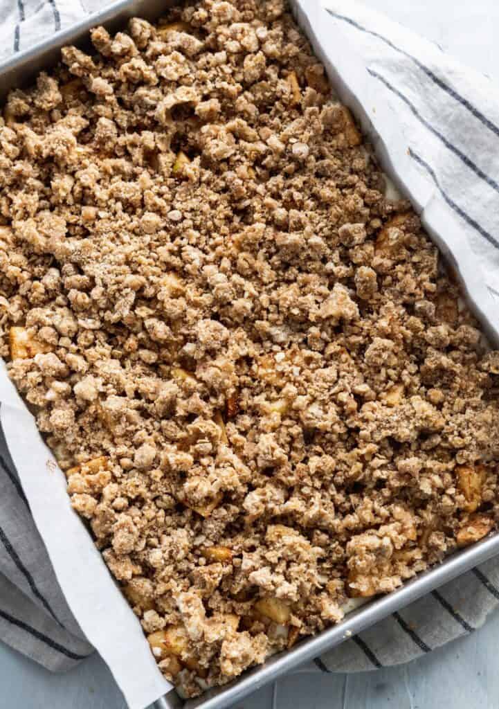 Cinnamon streusel on top of sliced apples in a metal pan.