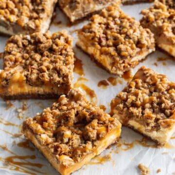 Cut up caramel apple cheesecake bars spread out on a parchment paper.