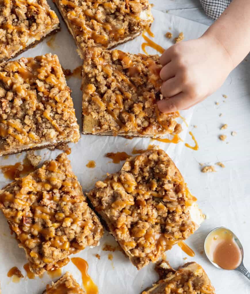 Caramel apple cheesecake bars with a toddler hand taking a bite.