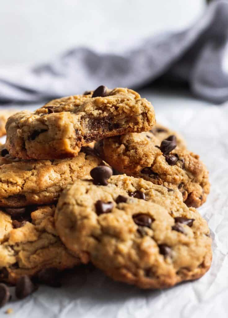 A pile of oatmeal peanut butter chocolate chip cookies with 1 cookie with a bite missing on top.