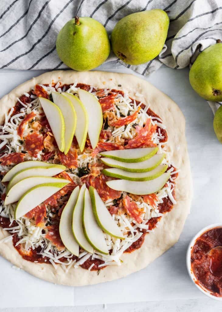 Raw pizza with sliced pears on top.