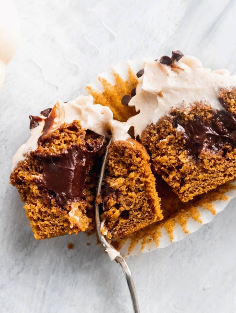 Chocolate stuffed pumpkin cupcakes split in half to see the chocolate filling.