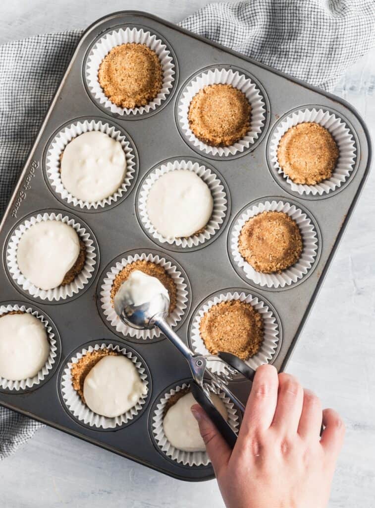 A cookie scoop plopping cream cheese batter over graham cracker crust.