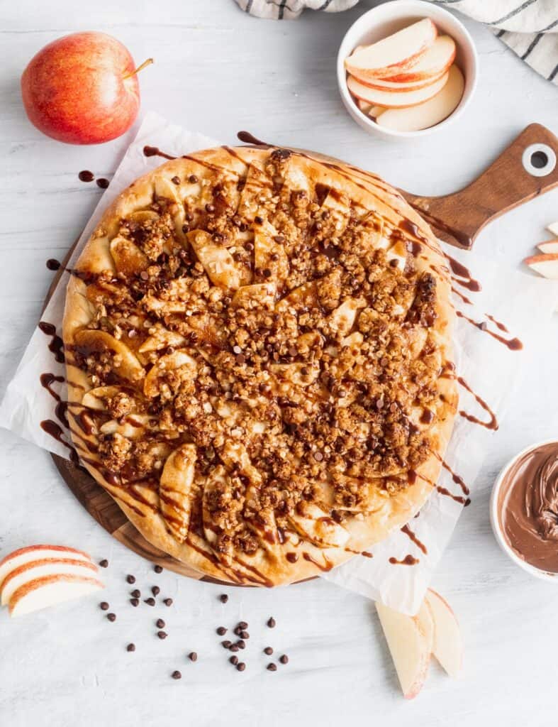 Apple Nutella dessert pizza on top of a wooden cutting board.