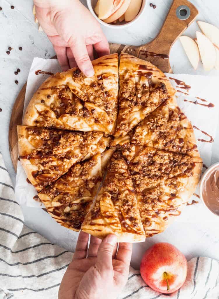 2 hands grabbing the apple Nutella dessert pizza.