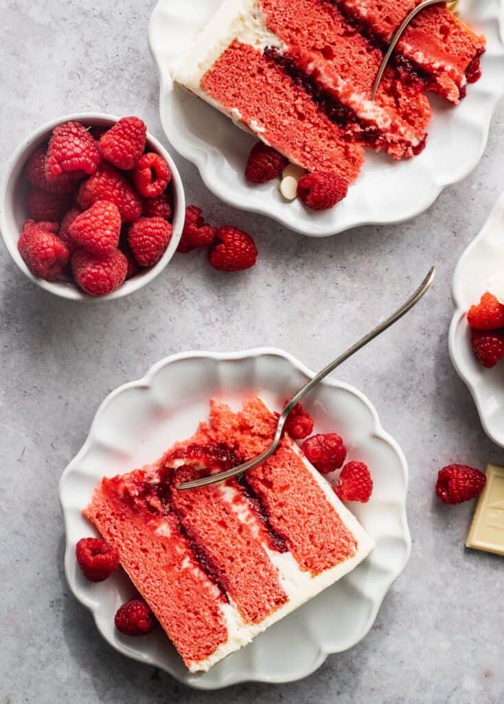 Slice of cake on 2 plates with a bowl of raspberries.