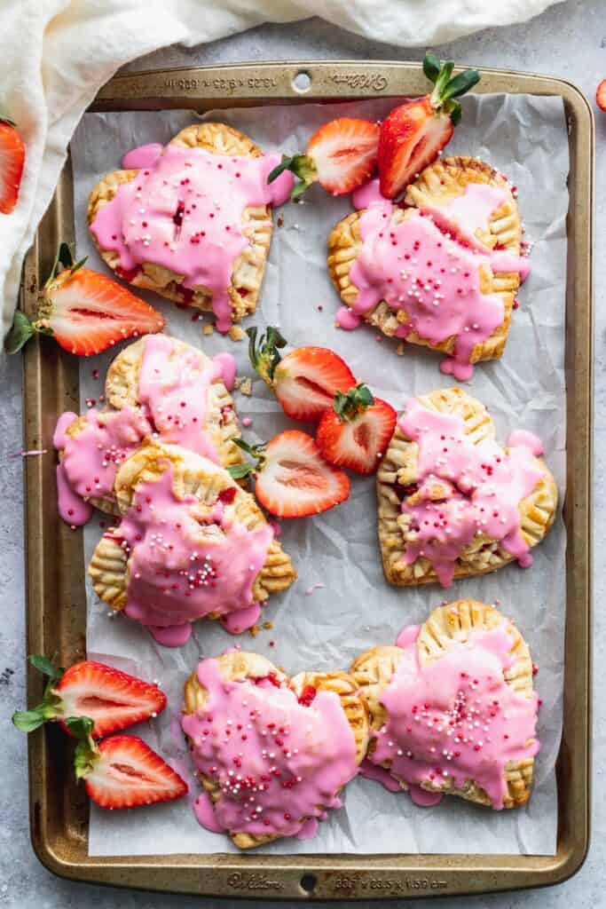 Strawberry hand pies with pink icing on a cookie sheet.