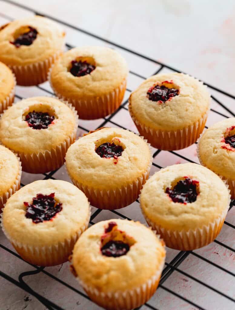 Filled cupcakes with jam on a wire rack.
