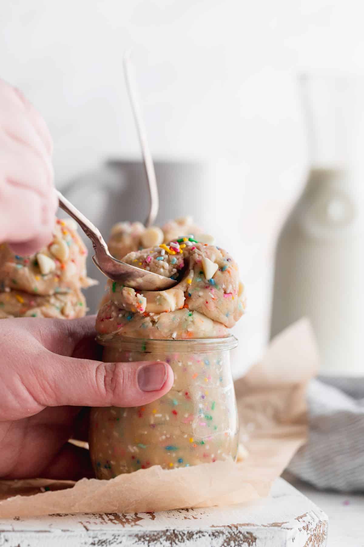 Hand holding funfetti edible cookie dough in glass.