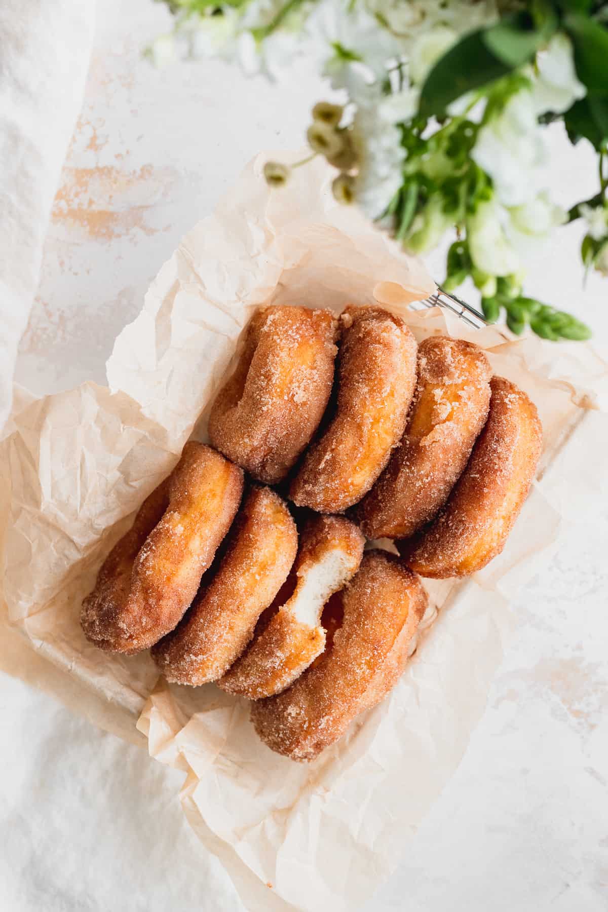 Cinnamon sugar doughnuts in a basket with flowers near by.