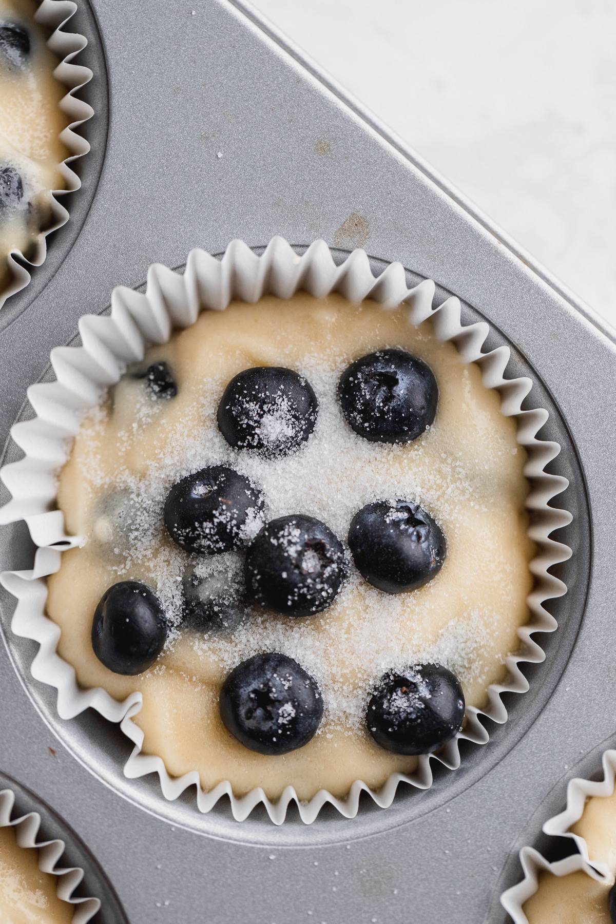 Batter in a muffin tin with sugar on top.