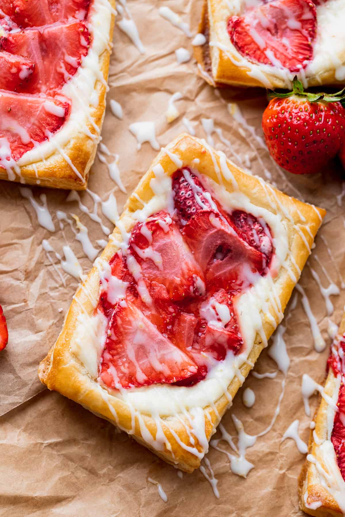 Strawberry danish on parchment paper with lemon glaze on top.