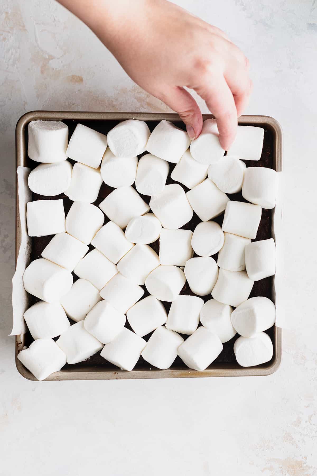 Marshmallows on top of the pan with a hand coming.