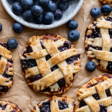 Mini blueberry pies with plate of blueberries.