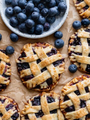 Mini blueberry pies with plate of blueberries.