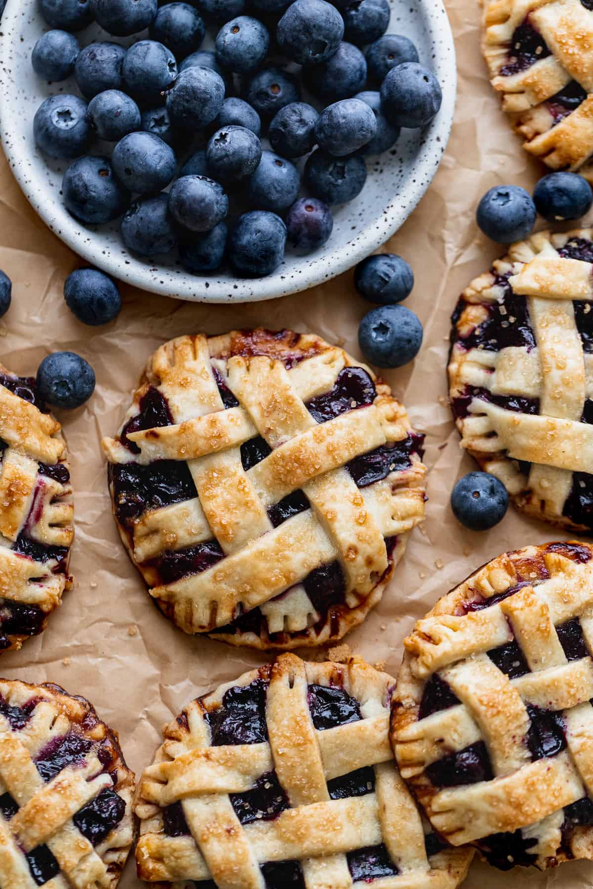 Mini blueberry pies with plate of blueberries.