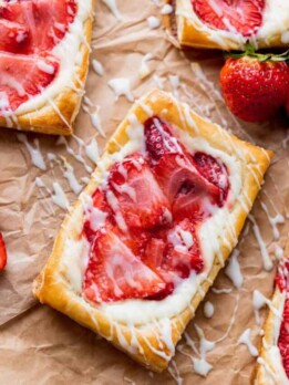 Strawberry danish on parchment paper with lemon glaze on top.