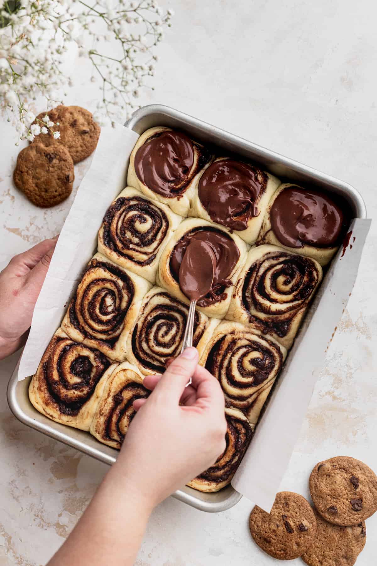 Spreading chocolate icing over the cinnamon rolls.
