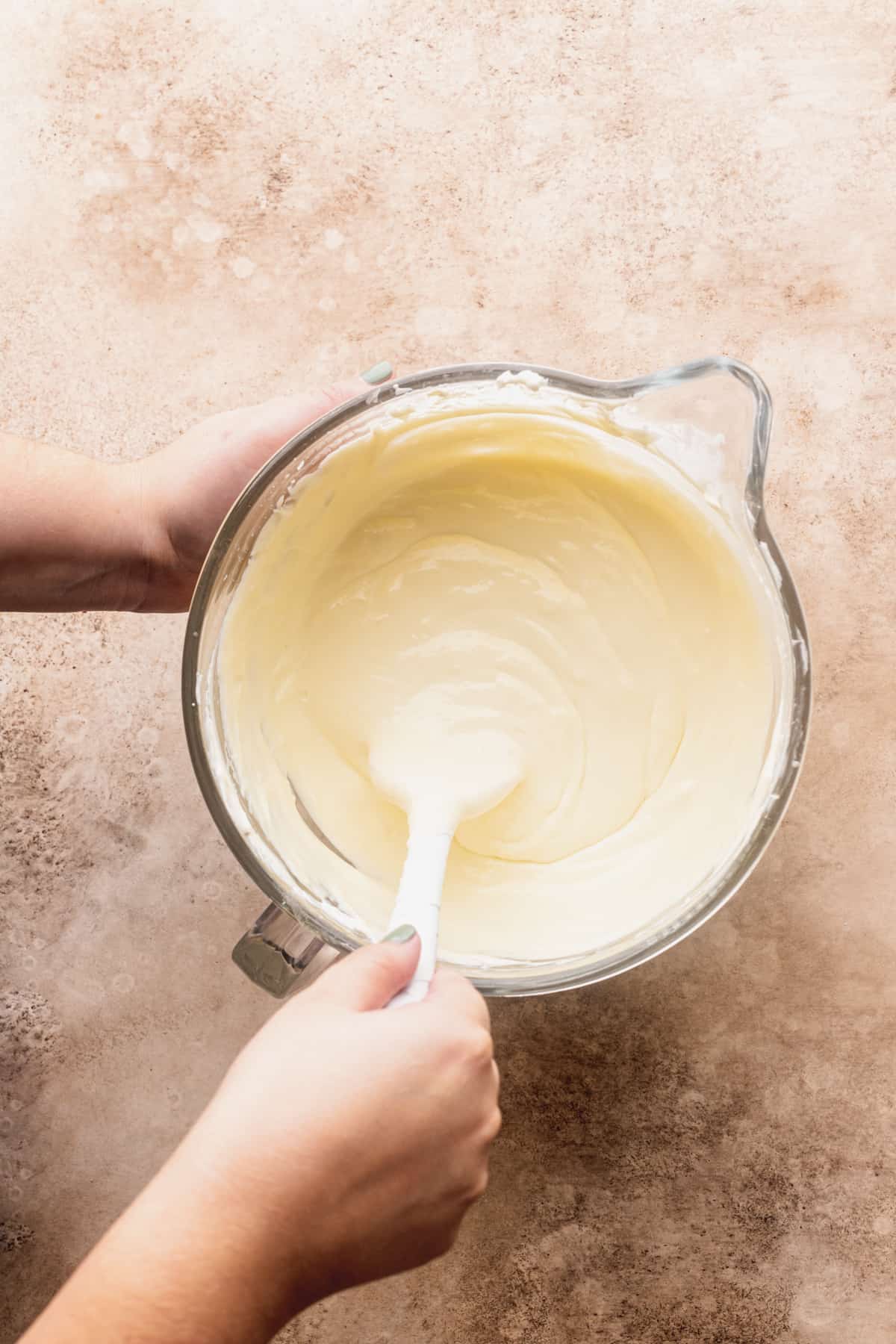 Mixing cheesecake batter in a glass bowl.