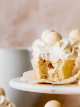 White chocolate truffle cupcakes with a bite missing on a cake stand.