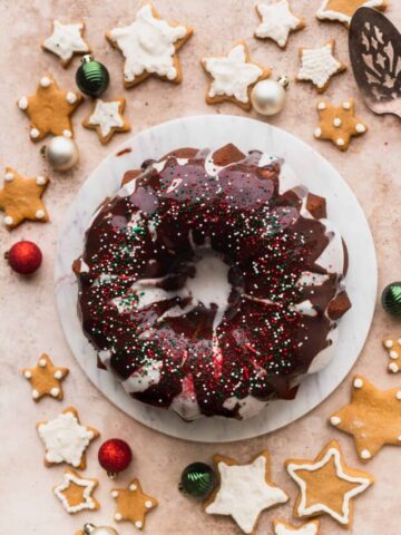Gingerbread bundt cake on a marble board surronded by gingerbread cookies.