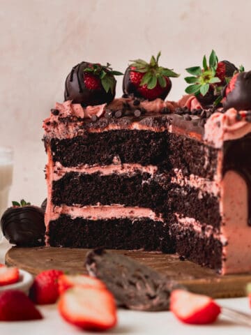 Chocolate covered strawberry cake cut open on a wood board.